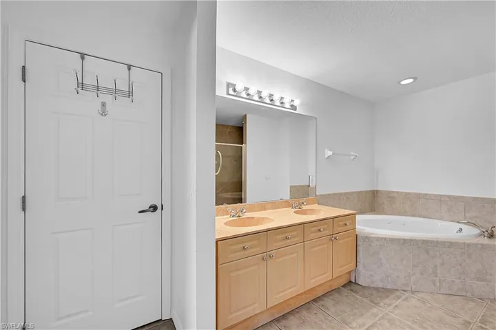 Bathroom featuring light tile patterned floors, a stall shower, a bath, and double vanity