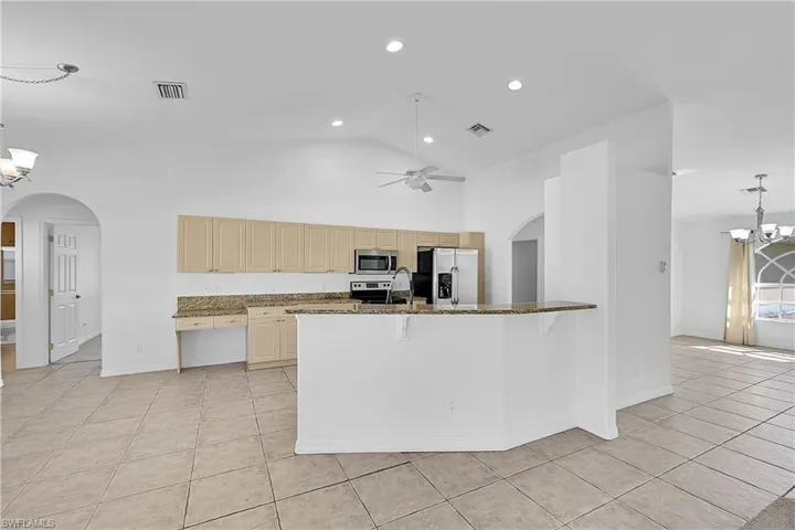 Kitchen with arched walkways, a chandelier, hanging light fixtures, appliances with stainless steel finishes, and dark stone countertops