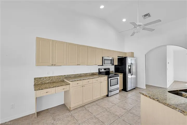 Kitchen featuring appliances with stainless steel finishes, light tile patterned flooring, high vaulted ceiling, light stone countertops, and arched walkways