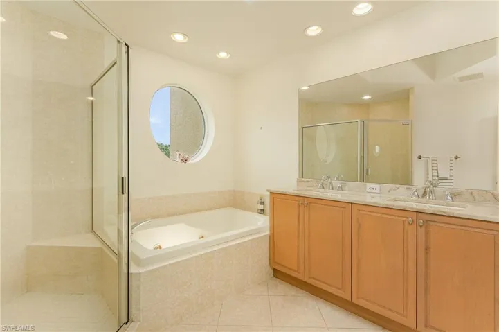 Bathroom featuring tile flooring, vanity with extensive cabinet space, shower with separate bathtub, and double sink