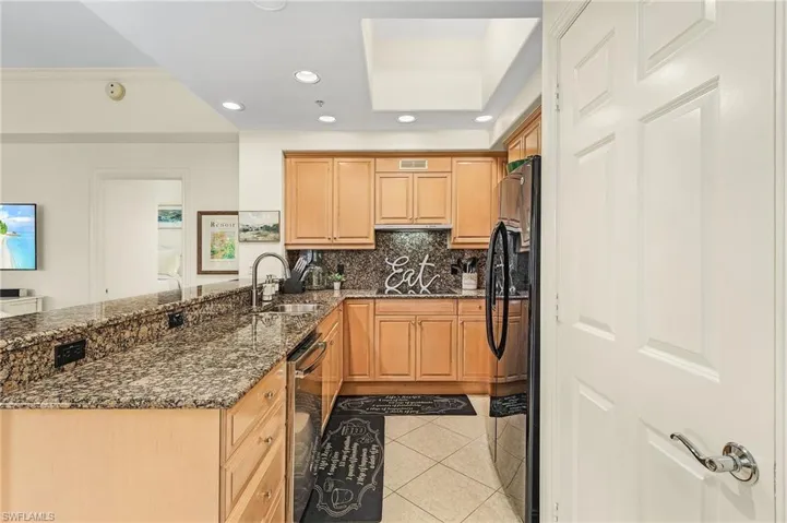 Kitchen with dark stone counters, backsplash, black refrigerator, sink, and light tile floors