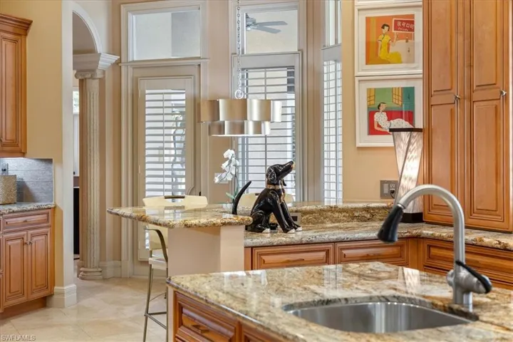 Kitchen with decorative columns, brown cabinetry, light stone countertops, and a sink