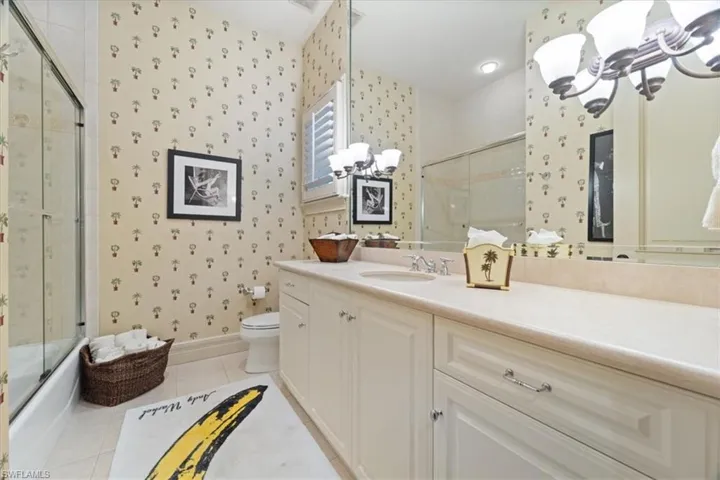Full bath with tile patterned floors, toilet, a chandelier, wallpapered walls, and vanity