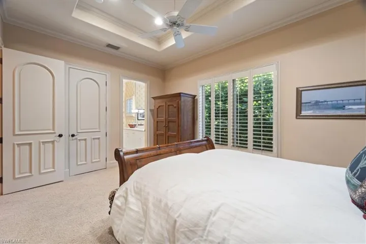 Bedroom with ensuite bathroom, visible vents, carpet, ceiling fan, and crown molding