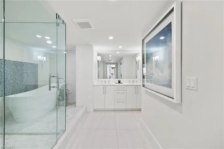 Full bath with double vanity, a stall shower, light tile patterned flooring, recessed lighting, and a freestanding bath