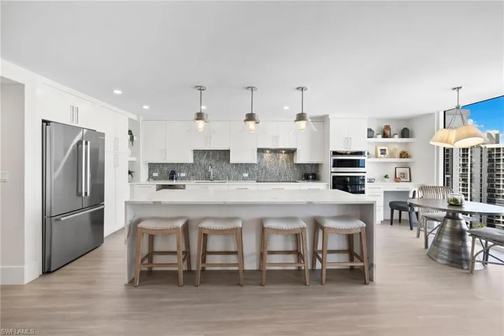 Kitchen featuring white cabinetry, stainless steel appliances, light stone countertops, a kitchen breakfast bar, and backsplash