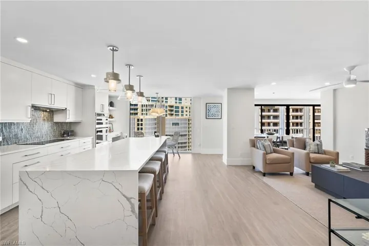 Kitchen with white cabinets, backsplash, hanging light fixtures, a kitchen bar, and light wood-style floors