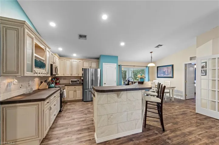 Gorgeous kitchen featuring upgraded cabinets, tumblestone backsplash, cabinet lighting, a tiled island with barstool seating and Samsung stainless steel appliances purchased in 2022