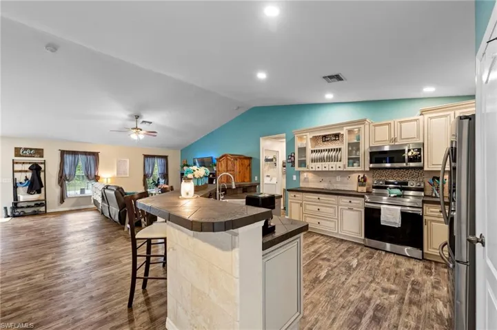 Gorgeous kitchen featuring upgraded cabinets, tumblestone backsplash, cabinet lighting, a tiled island with barstool seating and Samsung stainless steel appliances purchased in 2022
