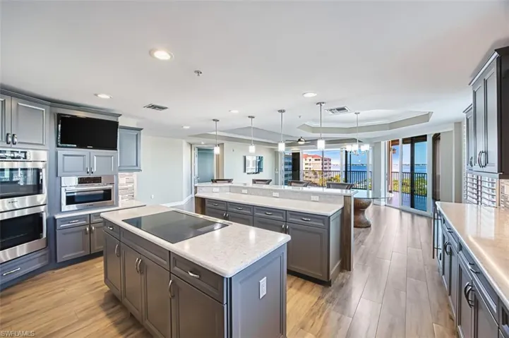 Kitchen with a tray ceiling, hanging light fixtures, light quartz countertops, stainless steel double oven, and black electric cooktop