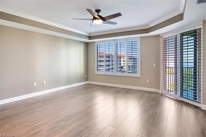 Unfurnished room with crown molding, a raised ceiling, wood like tile floors, and a ceiling fan