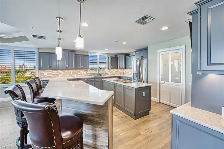Kitchen with decorative light fixtures, a kitchen island, light quartz countertops, stainless steel fridge with ice dispenser, and a kitchen breakfast bar