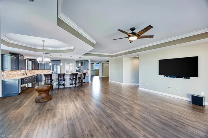 Living room featuring crown molding, a chandelier, a ceiling fan, dark wood tile floors, and a tray ceiling, open floor plan