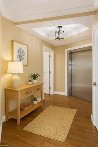 Hall featuring elevator, wood finished floors, crown molding, a chandelier, and a tray ceiling