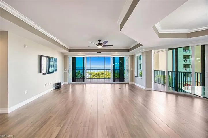 Unfurnished room featuring a raised ceiling, a wall of windows, wood finished floors, ceiling fan, and ornamental molding