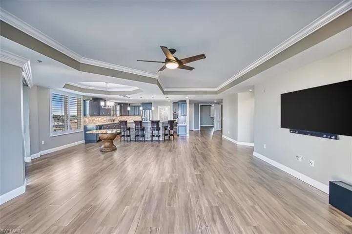 Living room with ornamental molding, ceiling fan, a chandelier, dark wood-type flooring, and a raised ceiling