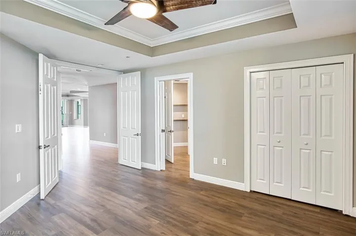 Second primary ensuite bedroom a raised ceiling, crown molding, dark tile wood-like floors, ceiling fan, and a closet