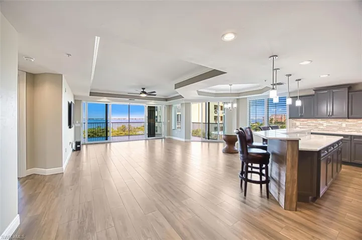 Kitchen featuring a tray ceiling, a breakfast bar area, open floor plan, dark wood-type flooring, and light stone countertops