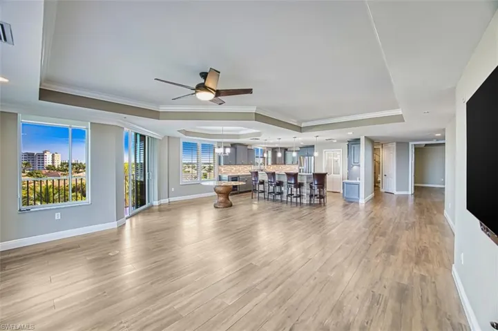 Living room with crown molding, a chandelier, a raised ceiling, light wood-style tile floors, and ceiling fan