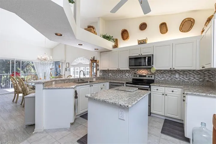 Kitchen with a peninsula, decorative light fixtures, light stone counters, stainless steel appliances, and a chandelier