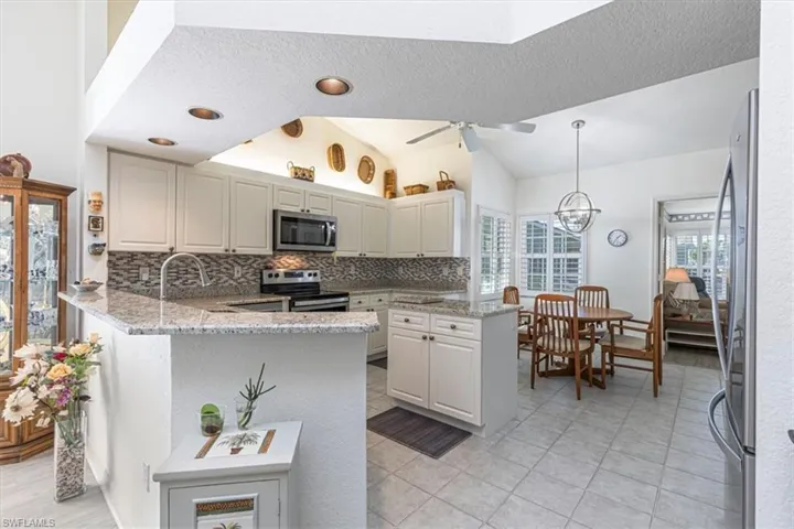 Kitchen with a peninsula, hanging light fixtures, light stone counters, stainless steel appliances, and backsplash