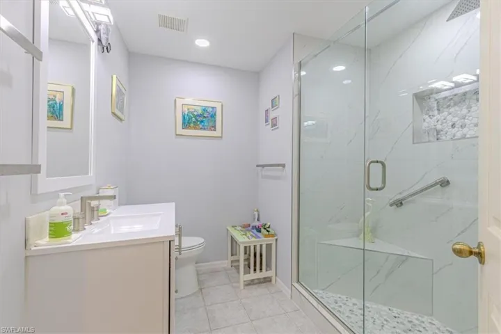 Bathroom with a marble finish shower, vanity, light tile patterned floors, and recessed lighting