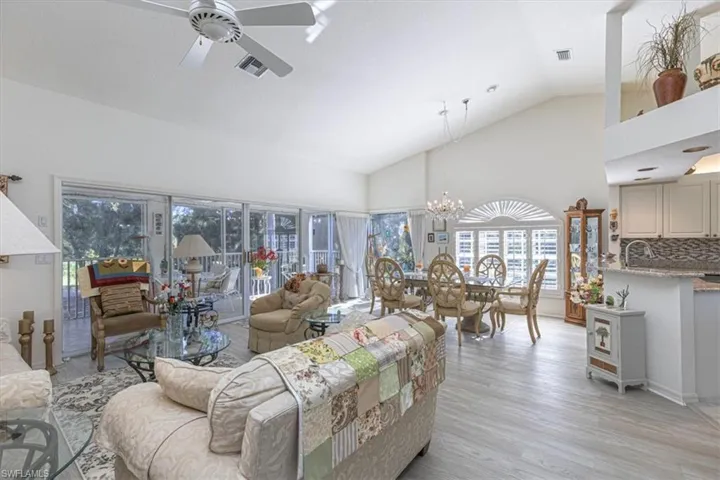 Living room with high vaulted ceiling, light wood-style flooring, plenty of natural light, a ceiling fan, and a chandelier