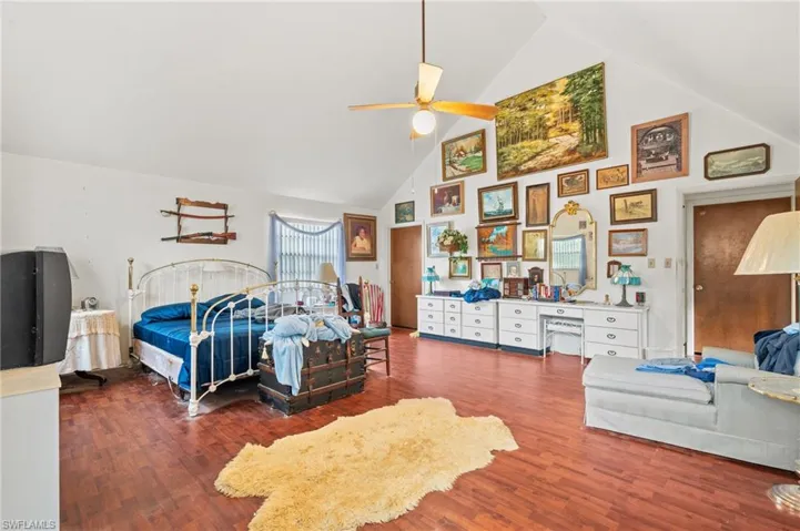 Bedroom with dark wood-type flooring, ceiling fan, and high vaulted ceiling
