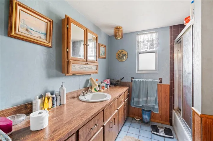 Bathroom with combined bath / shower with glass door, vanity, and tile patterned flooring