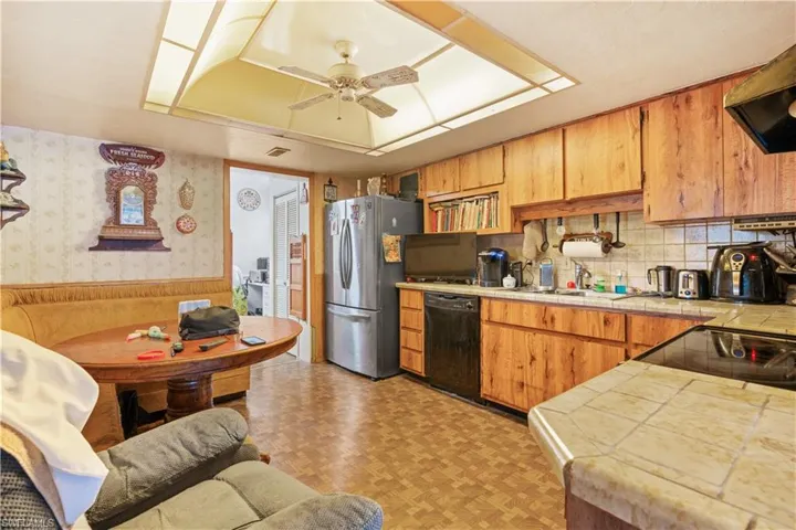 Kitchen featuring light parquet flooring, black dishwasher, stainless steel fridge, ventilation hood, and tile countertops