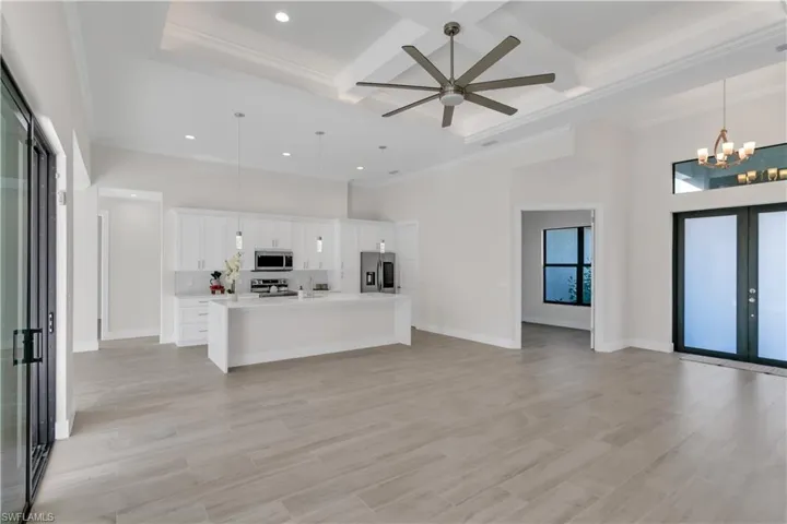 Kitchen featuring a towering ceiling, stainless steel appliances, decorative light fixtures, a center island with sink, and white cabinetry