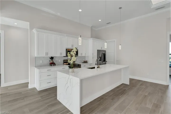 Kitchen featuring light stone countertops, white cabinetry, an island with sink, pendant lighting, and appliances with stainless steel finishes