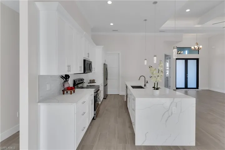Kitchen featuring white cabinetry, sink, stainless steel appliances, decorative light fixtures, and ornamental molding