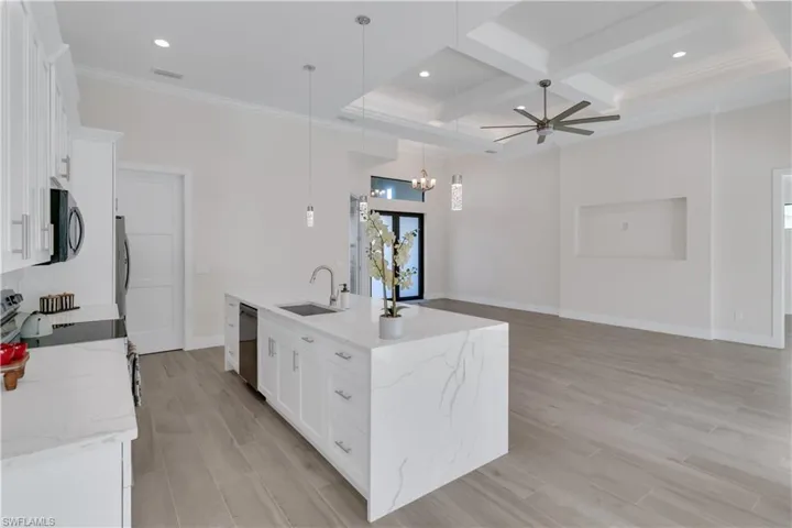 Kitchen featuring coffered ceiling, sink, decorative light fixtures, a center island with sink, and white cabinetry