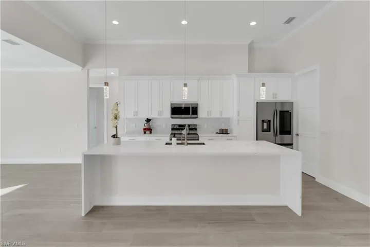 Kitchen featuring light stone countertops, sink, decorative light fixtures, white cabinets, and appliances with stainless steel finishes