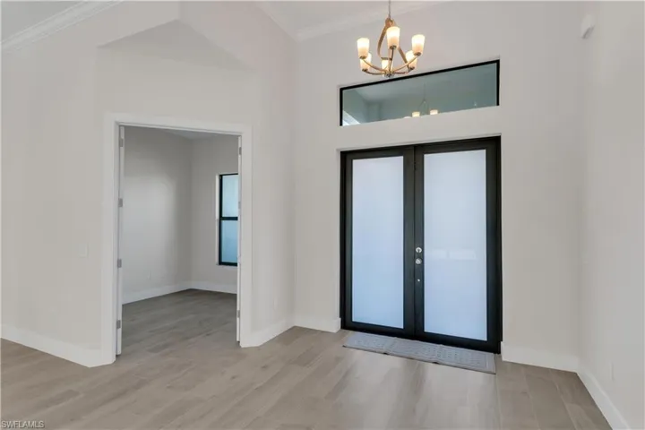 Foyer entrance with ornamental molding, light hardwood / wood-style flooring, french doors, and a notable chandelier
