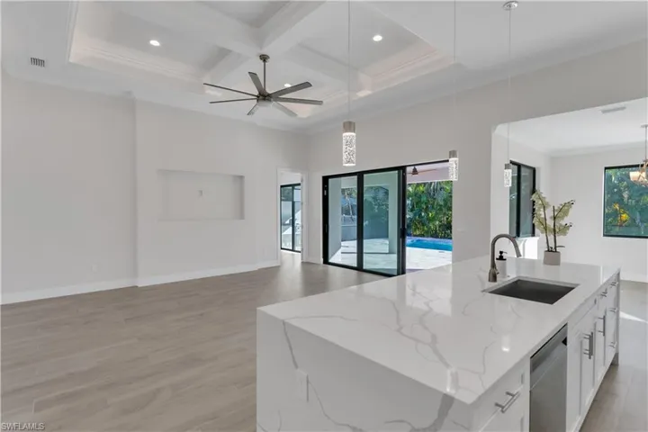 Kitchen featuring light stone counters, sink, decorative light fixtures, a center island with sink, and white cabinets