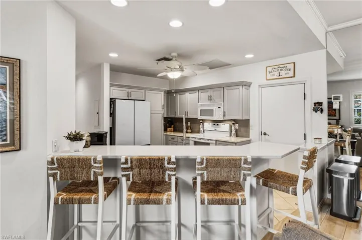 The beautifully updated kitchen blends style and functionality, showcasing quartz countertops, a farmhouse sink, new white cabinetry with soft-close doors and drawers, pull-out pantry shelving, a breakfast bar, a wine cooler, and a complete suite of white appliances. New refrigerator 2026.