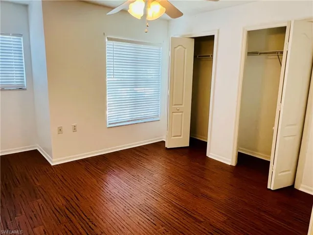 Unfurnished bedroom with ceiling fan, dark hardwood / wood-style flooring, and multiple closets