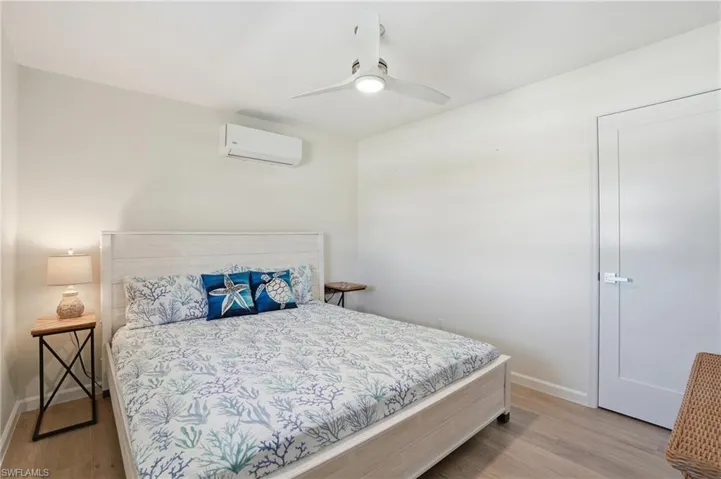 Bedroom featuring light wood tile floors, a ceiling fan, and a wall mounted air conditioner - Virtually Edited Image