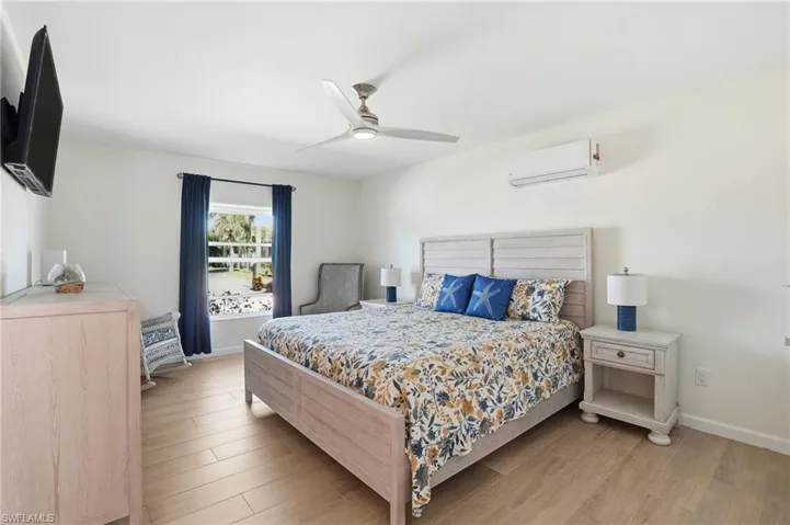 Bedroom with light wood tile floors, a ceiling fan, and a wall mounted air conditioner - Virtually Edited Image
