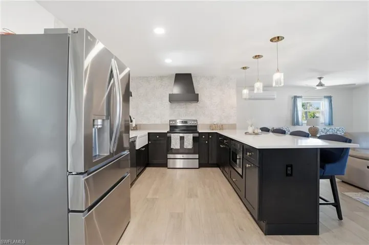 Kitchen with appliances with stainless steel finishes, a peninsula, a kitchen breakfast bar, dark cabinets, and decorative light fixtures - Virtually Edited Image
