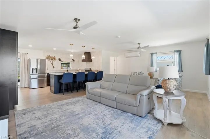 Living area with light wood tile flooring, a ceiling fan, and a wall mounted AC - Virtually Edited Image