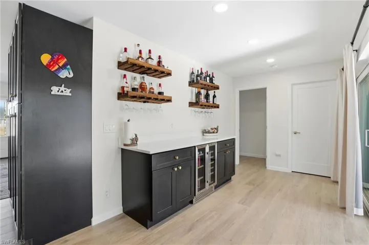 Indoor dry bar with open shelves, light wood-style floors, beverage cooler, recessed lighting, and dark cabinets - Virtually Edited Image