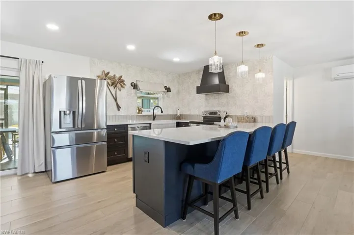 Kitchen featuring a peninsula, stainless steel appliances, a kitchen bar, pendant lighting, and light wood tile flooring - Virtually Edited Image