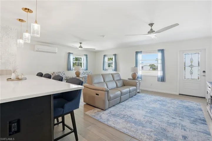 Living area featuring light wood tile flooring, a ceiling fan, and a wall mounted AC - Virtually Edited Image