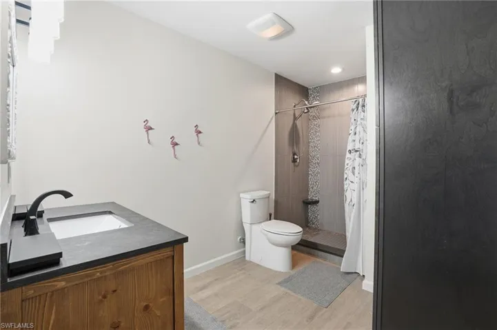 Bathroom featuring vanity, light wood tile floors, a tile shower, and recessed lighting - Virtually Edited Image