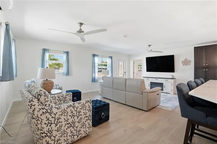 Living area featuring light wood tile finished floors, an AC wall unit, and a ceiling fan - Virtually Edited Image