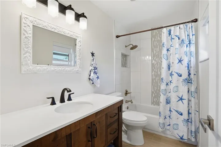 Bathroom featuring shower / bath combo with shower curtain, vanity, and light wood tile floors - Virtually Edited Image