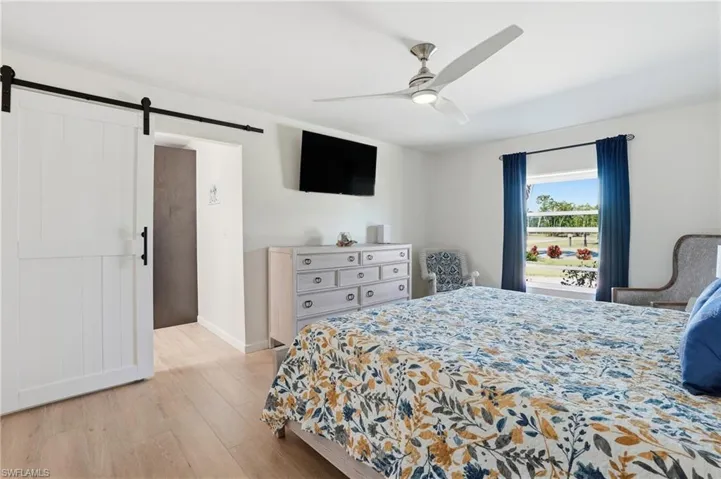 Bedroom featuring light wood tile flooring, a barn door, and ceiling fan - Virtually Edited Image